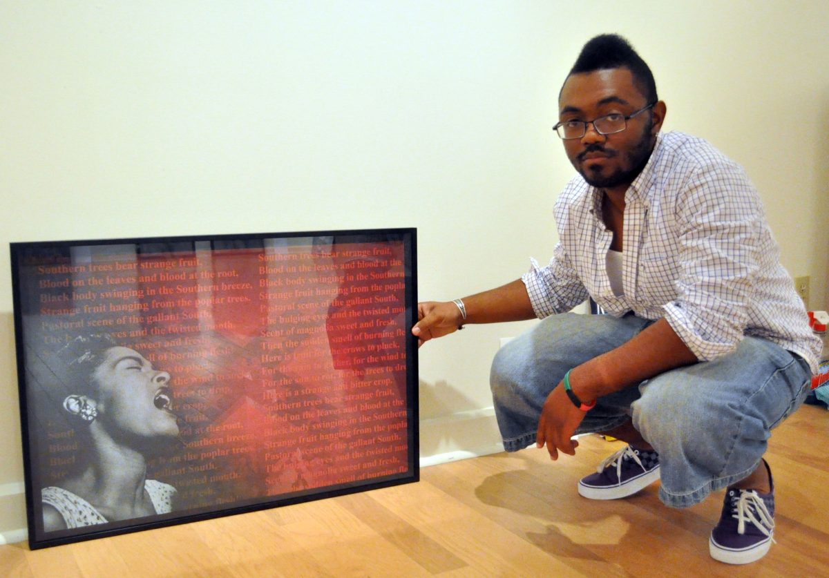 Southern graduate Rodrick Minor kneels next to his piece "Rotten Fruits in My Southern Garden" a computer graphic image/photo collage