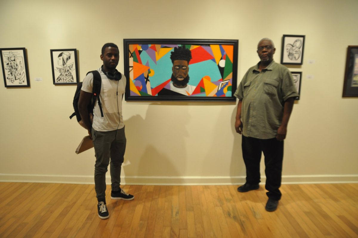 Assistant Professor Robert Cox and Senior Computer Science major Ricardo Figueiredo standing in front of Southern Alum Jade Meyers's art work entitled Black Ambiance Homecoming Alumni Art Gallery in Hayden Hall on October 14, 2015.