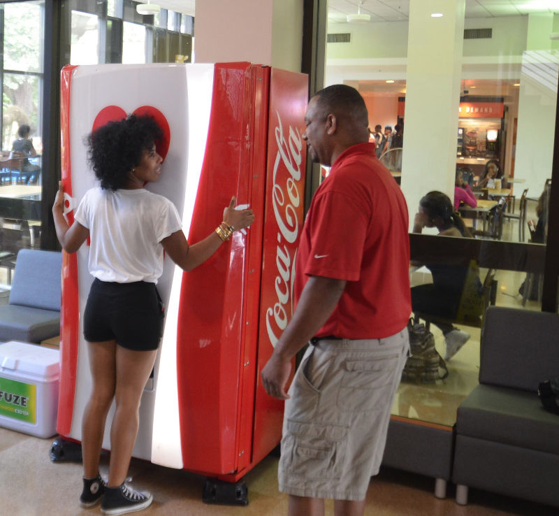 Coca-Cola business development manager Roderick Crockett looks on as Junior Mass comm major Tayla Cayette is the first to test Coca-Colas hug machine, Thursday September 22, 2016 in the Smith-Brown memorial student union.