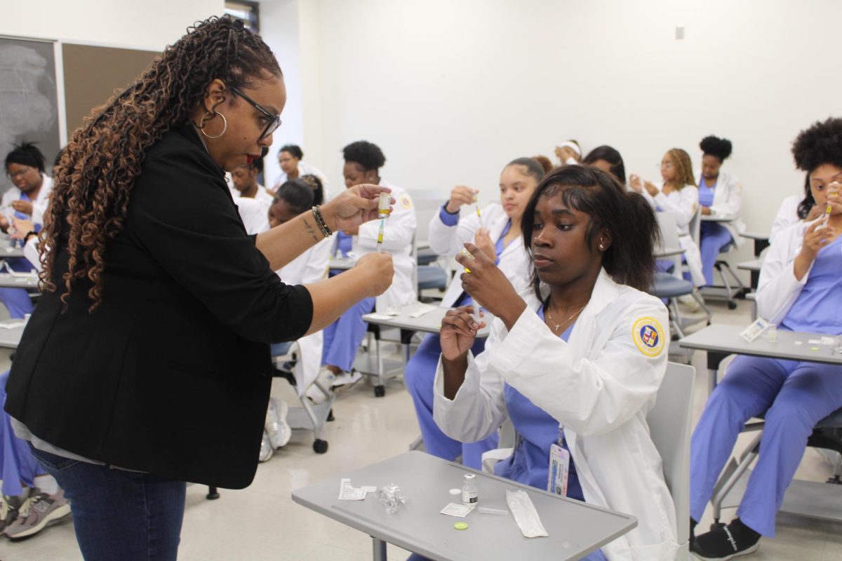 Assistant Professor of Nursing, Dr. Rosalynn Thyssen, coachs a nursing student on how to properly use a syringe before administering medication. 